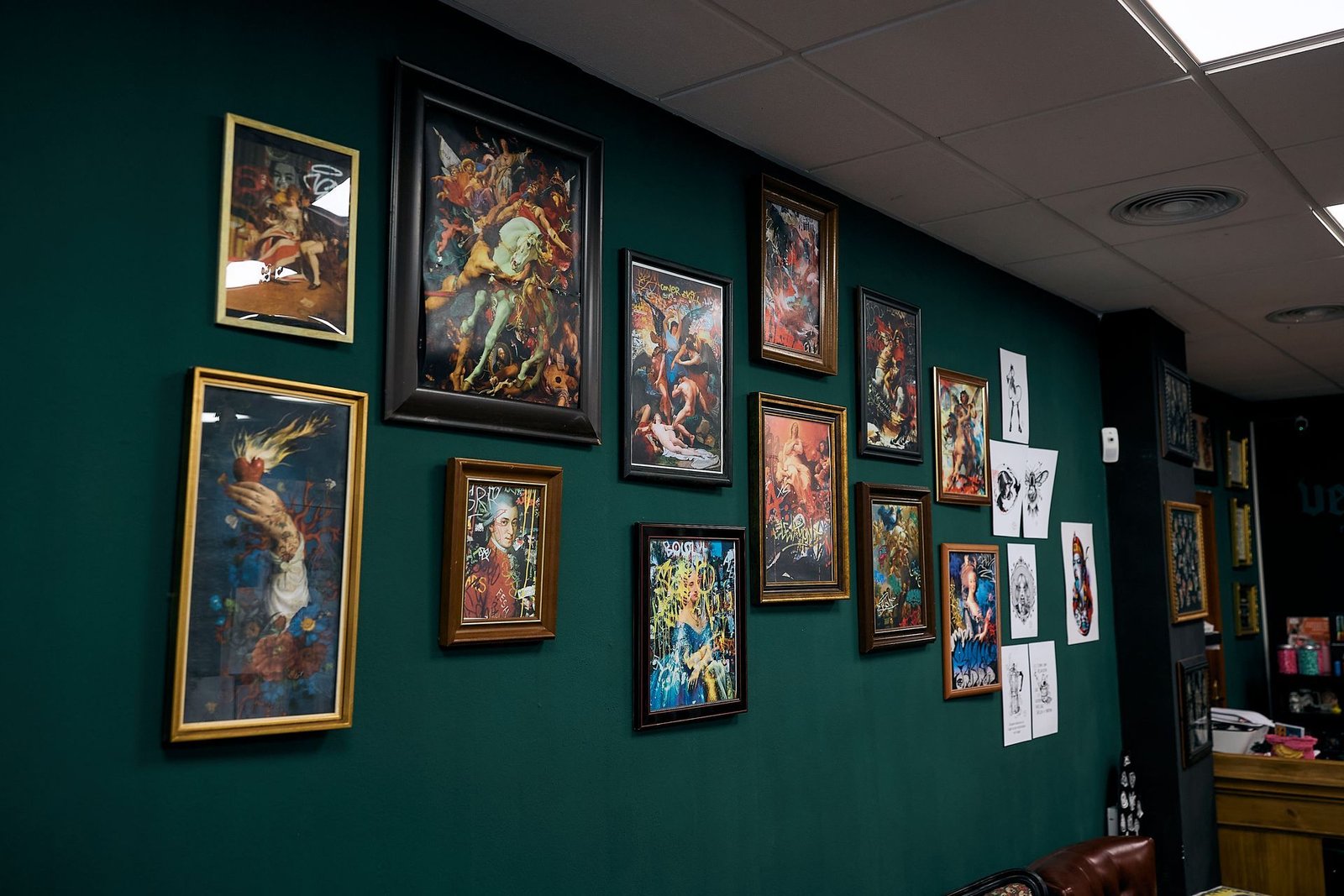 Obras de arte coloridas enmarcadas expuestas en una pared de galería de color verde oscuro en un pasillo.