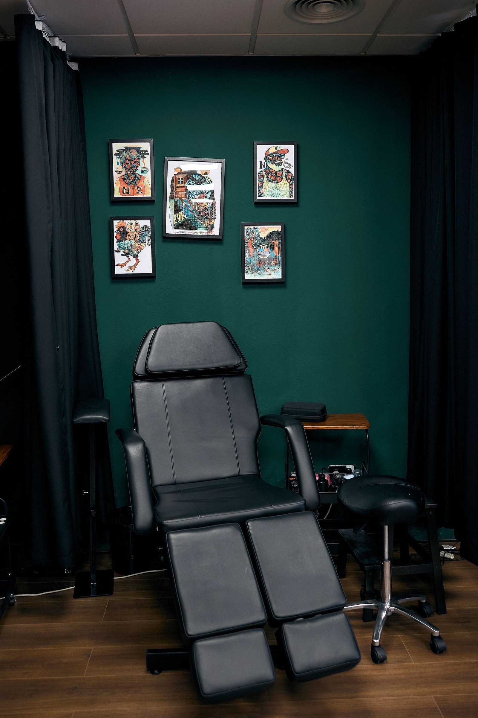 Sillón reclinable gris en una habitación pequeña con paredes verde oscuro, fotos enmarcadas y un taburete cerca.